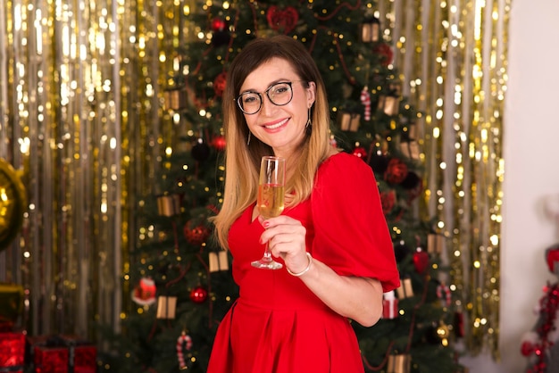 Happy beautiful adult middle aged woman is celebrating Christmas with glass of champagne