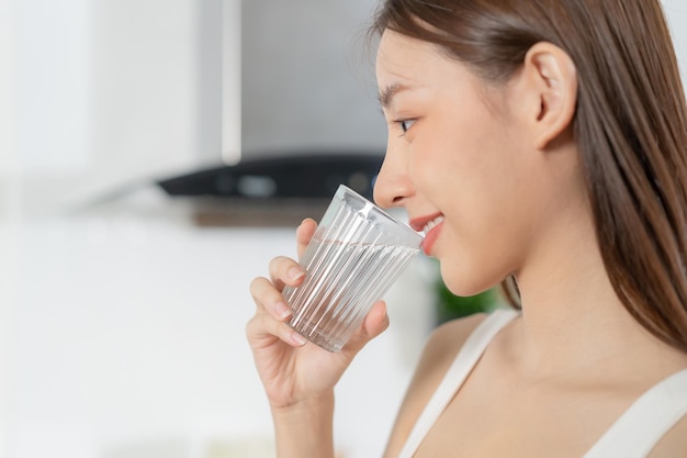 Happy beautiful asian thirsty young woman girl drinking sip fresh glass of water for hydrate holding transparent glass in her hand thirsty at home Health care healthy lifestyle concept