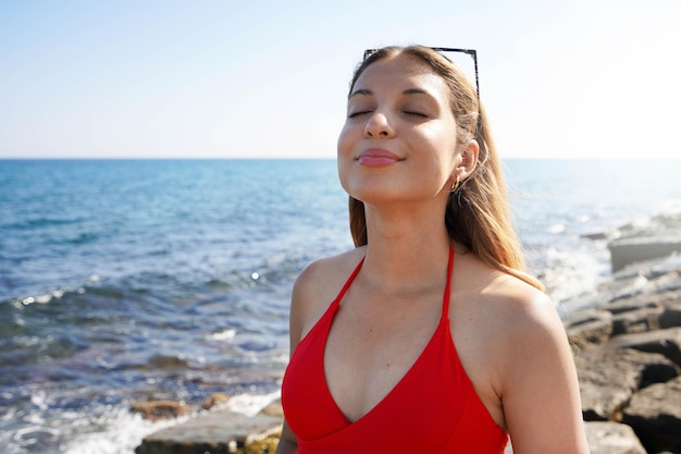 Happy beautiful carefree woman breathing fresh air enjoying wind on the beach Relaxed bikini woman with closed eyes feeling good and free outdoor