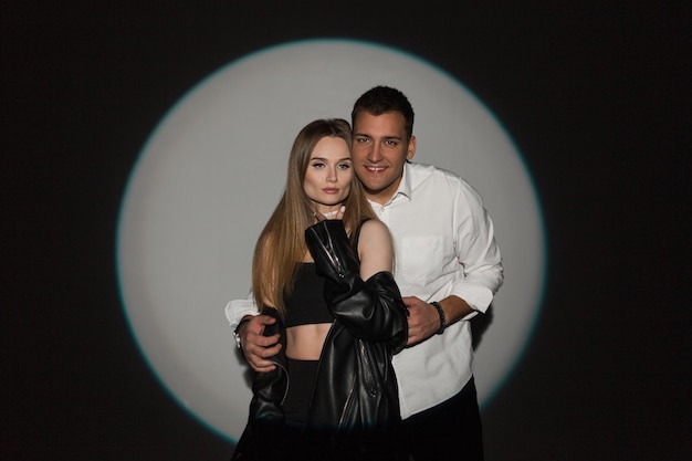 Happy beautiful couple girl and handsome man in fashionable casual clothes on a dark background in a light circle