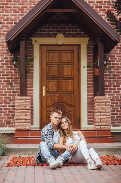 Happy beautiful couple sitting at the blanket carpet in front of the new home