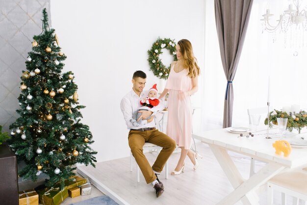 Happy beautiful family with baby in little Santa costume celebrate Christmas