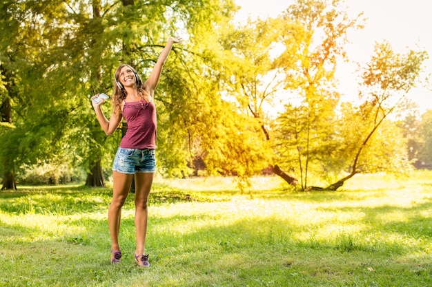 Happy beautiful girl enjoying music on headphones in the sunny park.