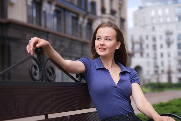 Happy beautiful girl young woman is sitting on bench in the yard of her new house home apartment in the city smiling enjoying summer day