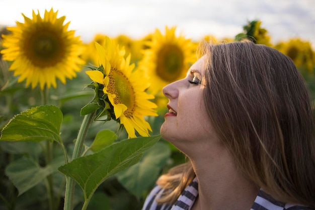 Happy beautiful middle aged woman rejoices and enjoys sunflower field blooming on a sunny day