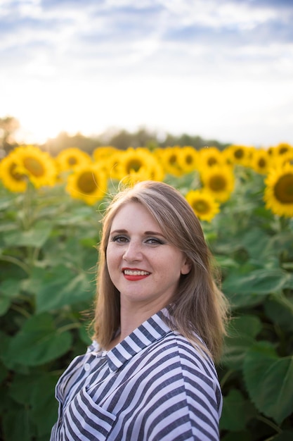 Happy beautiful middle aged woman rejoices and enjoys sunflower field blooming on a sunny day