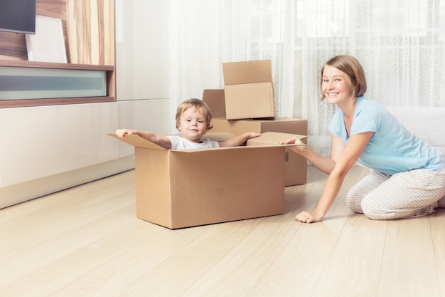 Happy and beautiful mother and child family together in a new home with cardboard boxes