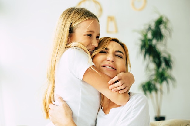 Happy beautiful mother and daughter spending time together, hugging and have a fun while sitting on the couch at home. Family concept