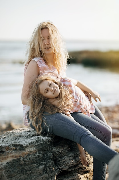 Happy beautiful mother and her daughter having fun on the rocky beach at sunset.