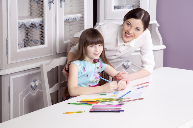 Happy beautiful mother teach her daughter to paint, painting and smiling and looking at camera. Studio shot.