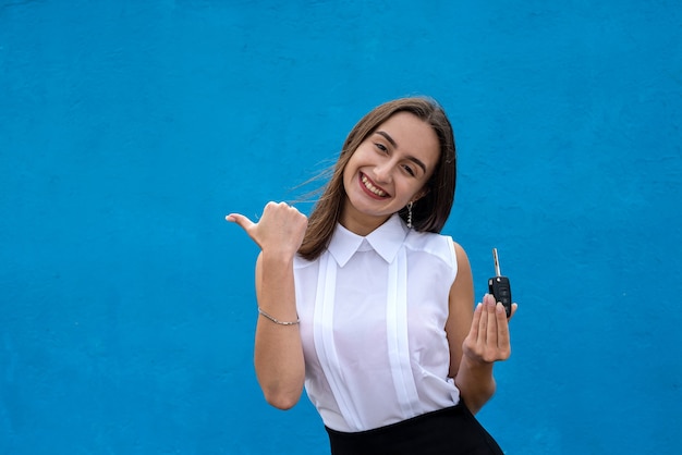 Happy beautiful saleswoman with a keys car on blue background