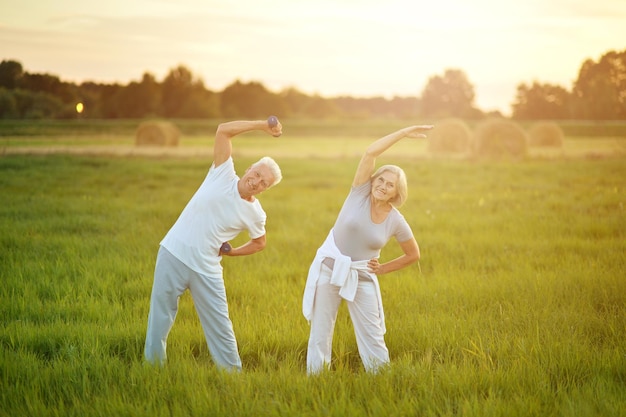 Happy beautiful senior couple exercising in summer field