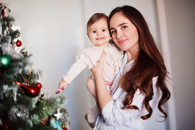 Happy beautiful woman having fun with her little daughter near the Christmas tree