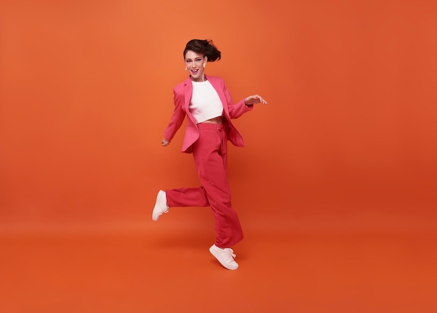 Happy beautiful woman smiling and jumping while celebrating success isolated over orange background