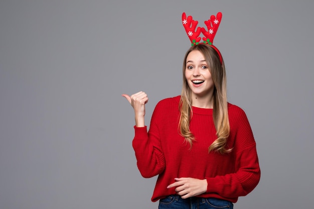 Happy beautiful woman with reindeer horns on her head looks pointed side on gray wall