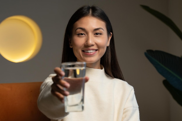 A happy beautiful young asian woman holding a clear glass of clean water in her hand and looking at