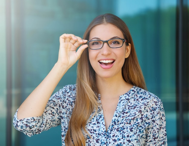 Happy beautiful young woman holds her glasses and looks at camera outdoor 