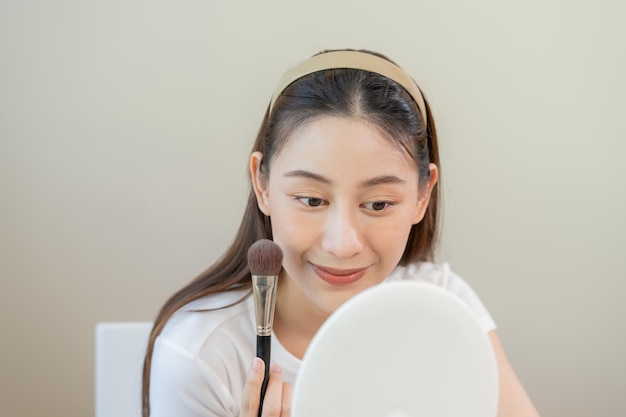 Happy beauty blogger concept cute asian young woman girl smile make up face by applying brush blush powder on her cheek looking at the mirror People look with natural fashion style copy space