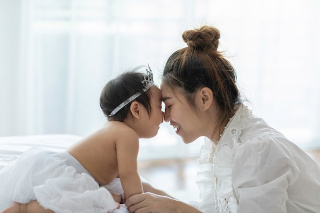 Happy Beauty mother Holding Cute Sweet Adorable Asian Baby wearing white dress smiling and playing with happiness emotional in cozy bedroom,Healthy Baby Concept,Selective Focus