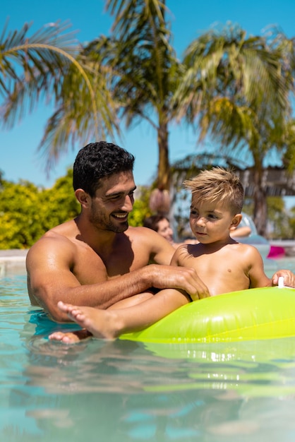 Happy biracial father and son playing together in swimming pool. Spending quality time, lifestyle, family, summertime and vacation concept.