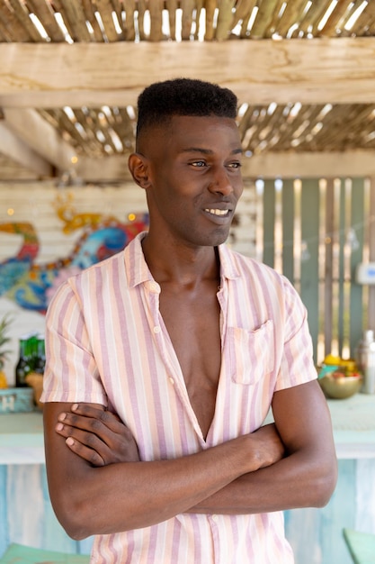 Happy biracial man standing in sunny beach bar smiling and looking away, unaltered. Small business, summer, relaxation, refreshment and vacation.