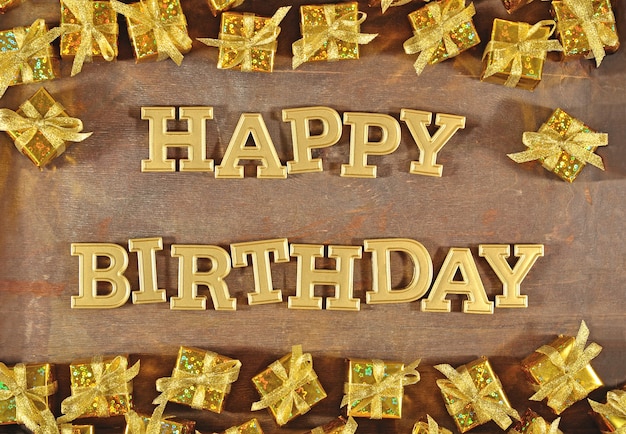 Happy birthday golden text and golden gifts on a wooden background