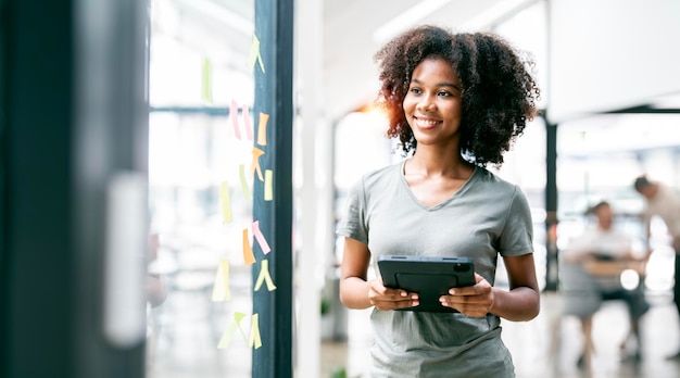 Happy black businesswoman holding tablet standing in a creative office