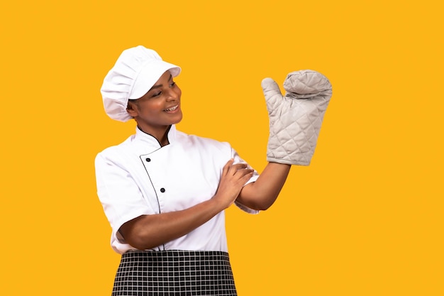 Happy black chef woman looking at oven mitt on her hand