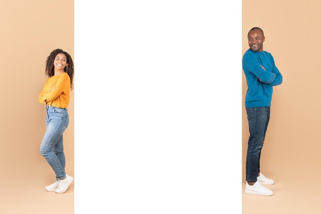 Happy black couple posing near white advertisement board demonstrating free copy space for your design