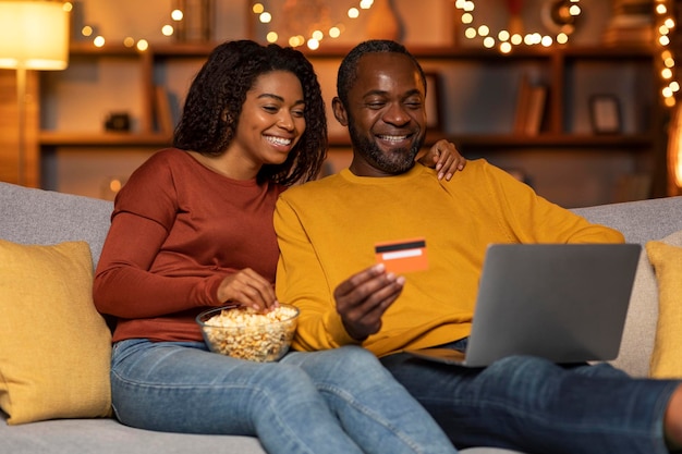 Happy black couple shopping from home using laptop credit card