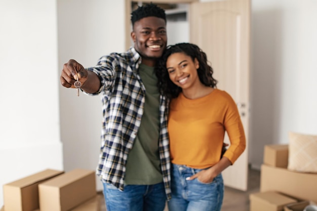 Happy black couple showing new house key embracing at home