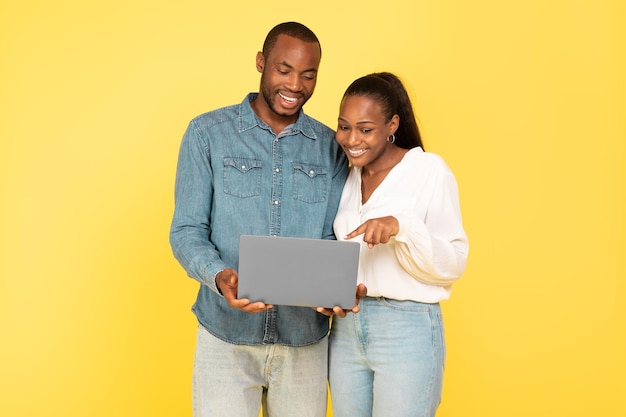 Happy Black Couple Using Laptop Together Over Yellow Studio Background