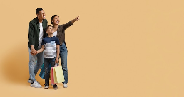 Happy black family enjoying shopping together pointing at copy space