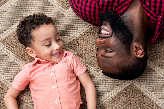 Happy black father and son lying on floor