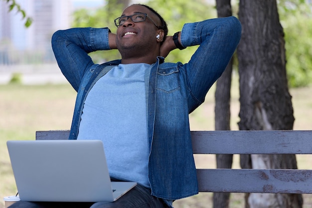 Happy black guy sits on a park bench waiting for his first date