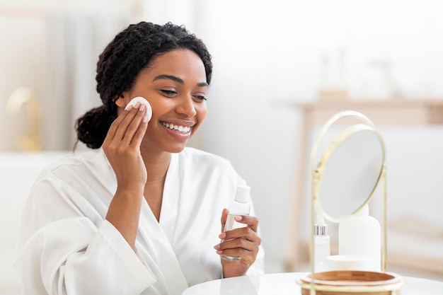 Happy Black Lady Using Micellar Water And Cotton Pad For Skin Cleansing