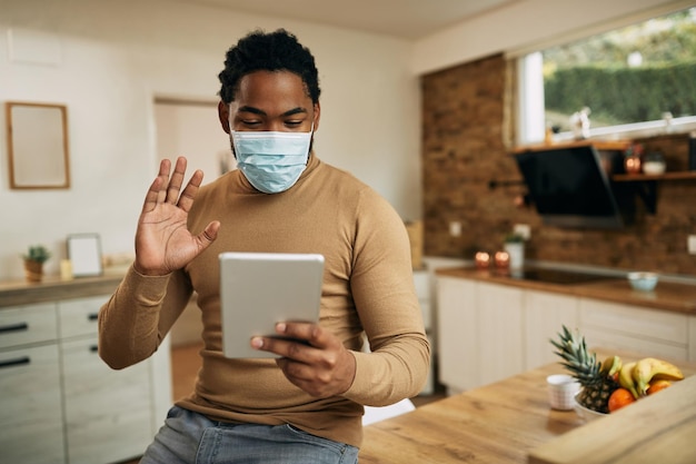 Happy black man waving during video call over touchpad at home during COVID19 pandemic