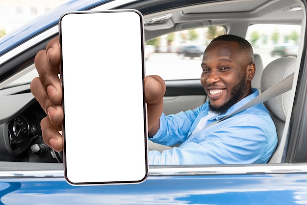 Happy black man with blank smartphone in hand sitting in luxury car