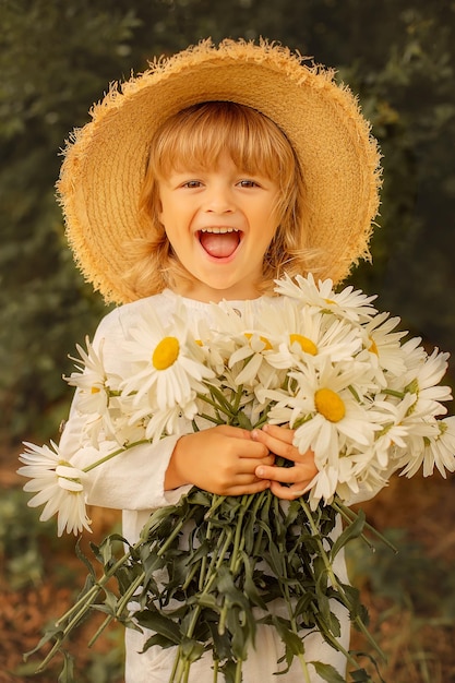 happy blond boy in a white linen suit straw hat and daisies in his hands