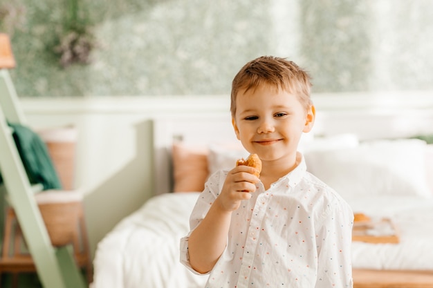 Happy blond preschooler eating croissant at home. Houses. Childhood.