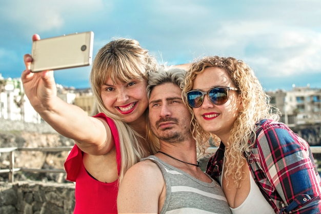 Happy and blond young people taking a selfie with their smartphone outdoors