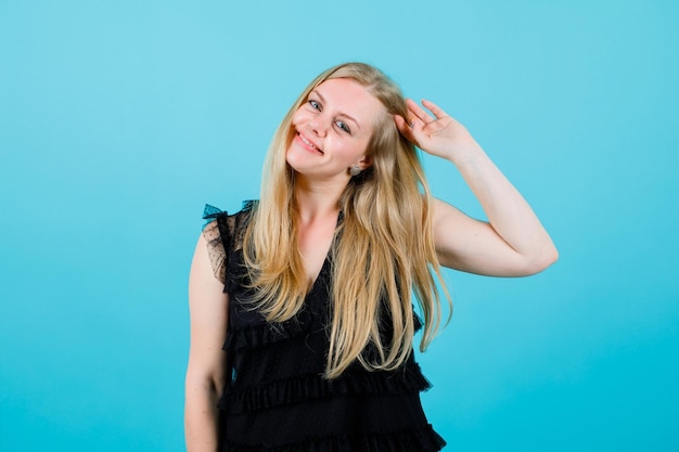 Happy blonde girl is holding hair on blue background