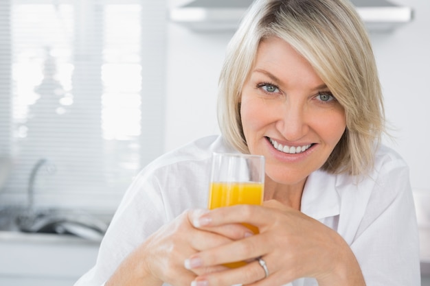 Happy blonde having orange juice in kitchen