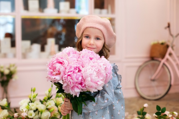 happy blonde little girl with long curly hair and in a beret with bouquet of pink peonies.