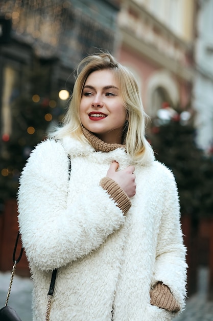 Happy blonde model wears winter coat and black purse walking at the city