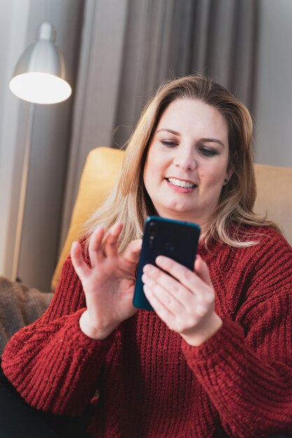 Happy blonde woman at home using smartphone