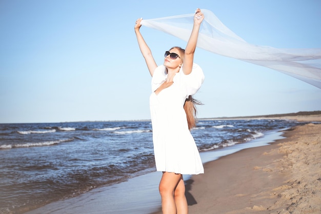 Happy blonde woman is catching clouds and wind with her arms on the ocean beach