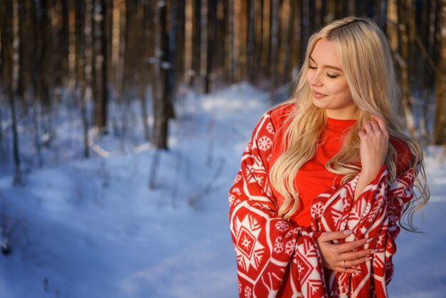 Happy blonde woman in red sweater in winter forest