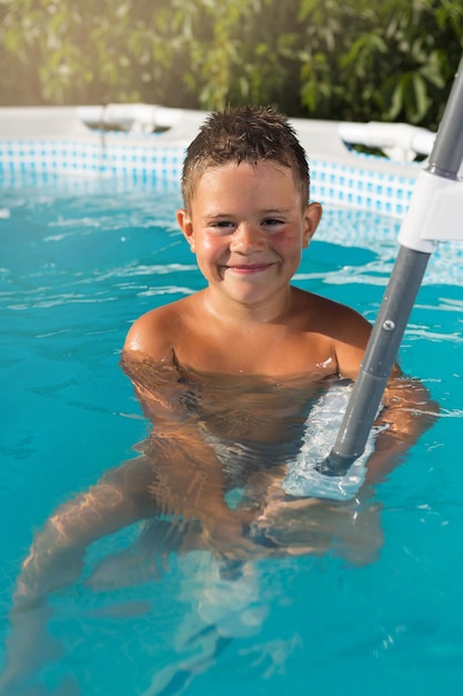 Happy boy in the blue water pool boy sitting in the water and holding on to the stairs concept