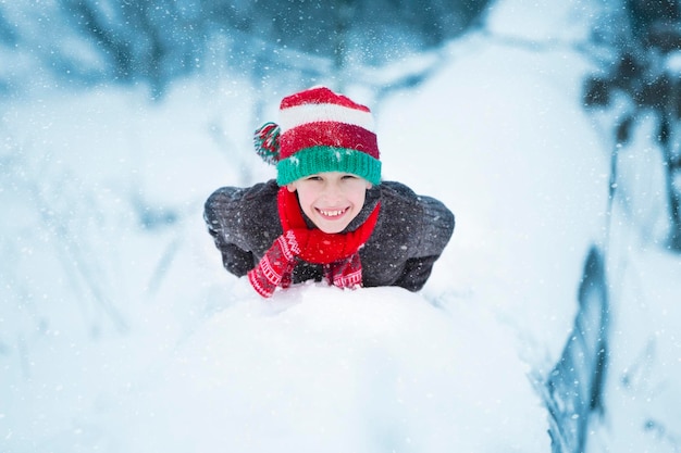 A happy boy in a Christmas hat lies on the snow and smiles